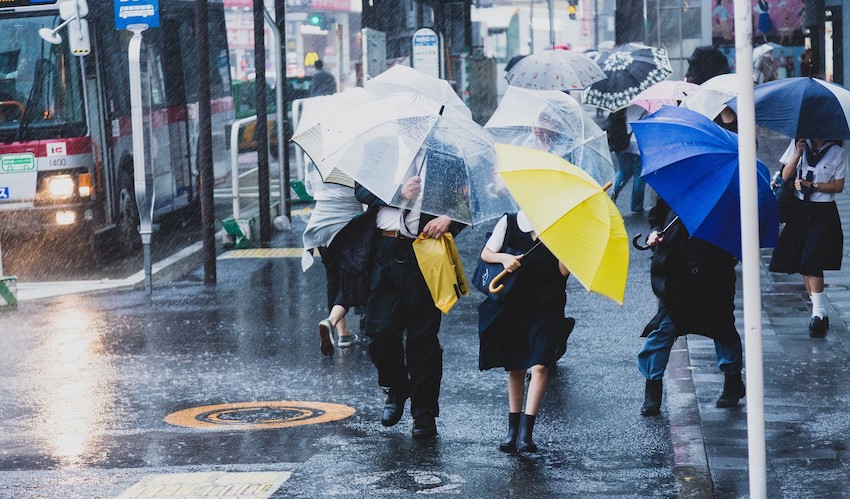 台風で突風が吹く駅前と必死に傘をさす人々